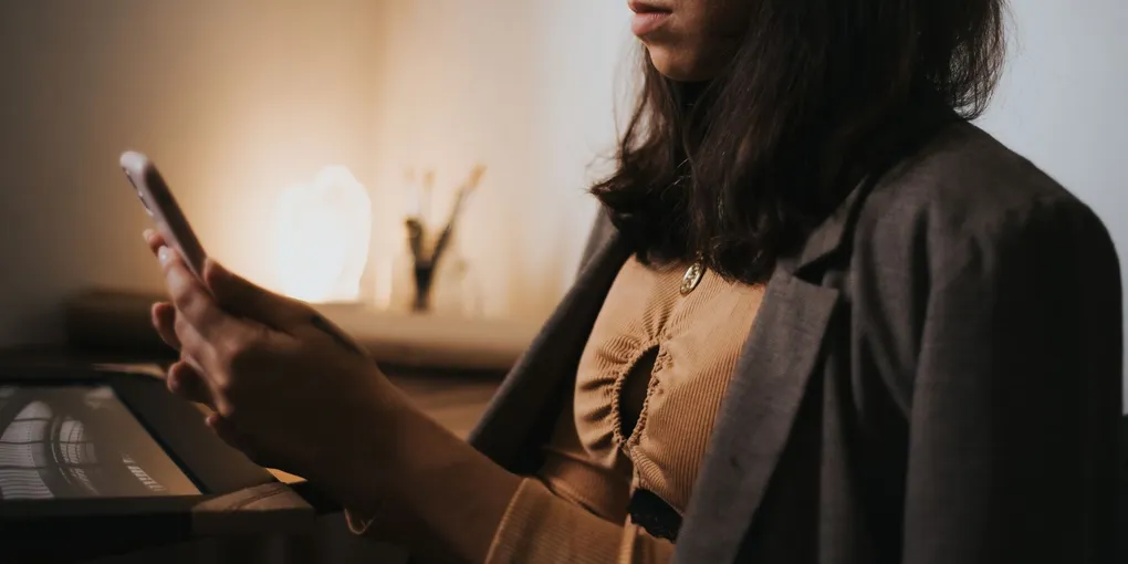 Mulher com o corpo tenso olhando para o celular em ambiente de trabalho